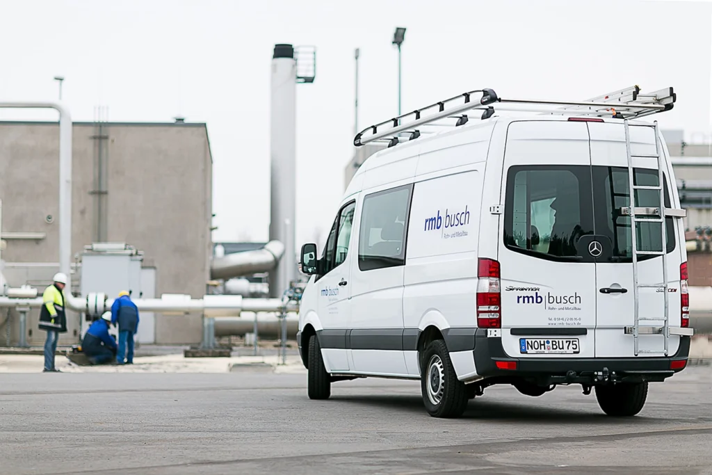 Servicefahrzeug von rmb busch auf einem Anlagengelände, im Hintergrund arbeiten Monteure an einer Rohrleitung